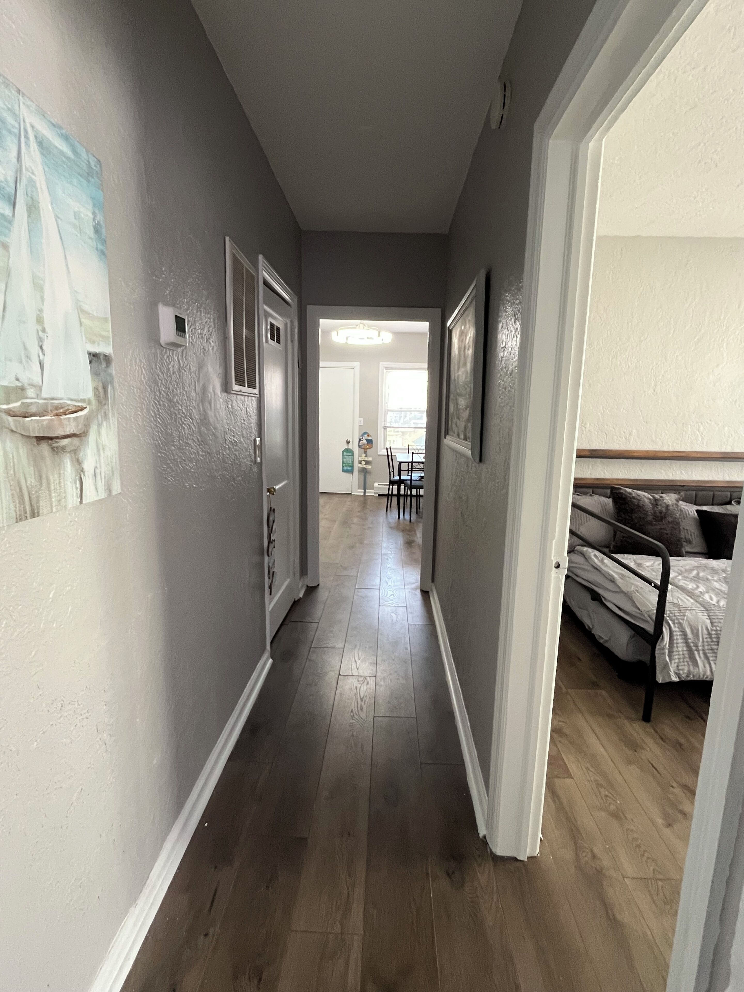 A hallway with a bed, a dining area, and a door leading to another room.
