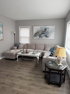 Ein Wohnzimmer mit Sofa, Hocker, Couchtisch, Lampe und Kunstwerken.
