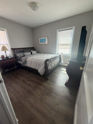 A bedroom with a bed, nightstand, lamp, and a picture on the wall.