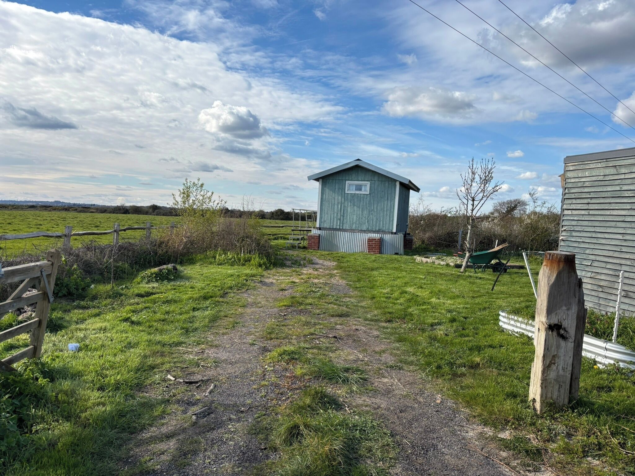 Ein ländliches Anwesen mit einem Kiesweg, der zu einer Holzhütte führt, umgeben von viel Grün und blauem Himmel.