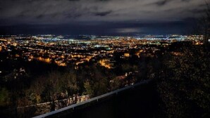 Paesaggio urbano notturno con vista sulle luci della città e un cielo nuvoloso.