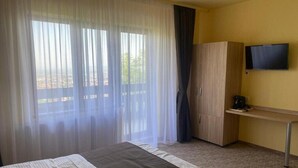 Una camera d'albergo con un letto, una scrivania, una televisione e una finestra con tende leggere.