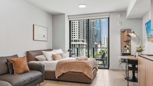 A modern bedroom with a bed, a sofa, a balcony with a view of buildings, and a small kitchenette. - Chic Studio | Free parking | Steps to PAMM (Miami)