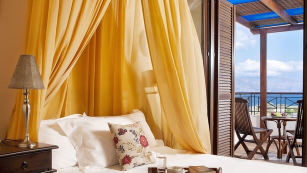 Una cama con cortinas amarillas, una lámpara de noche y una bandeja con un vaso de agua y un libro.
