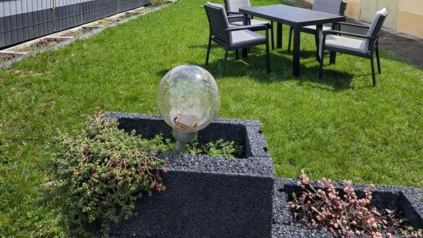 A backyard with a table and chairs, a decorative glass sphere, and a stone planter with plants. - Frankfurt Airport view apartments (Moerfelden-Walldorf)