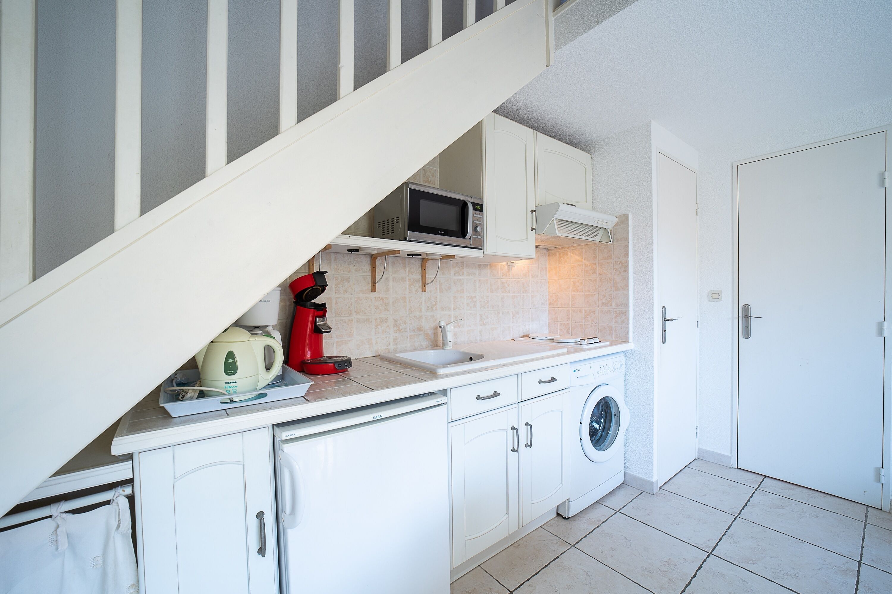 A compact kitchen with a microwave, coffee maker, and washing machine.
