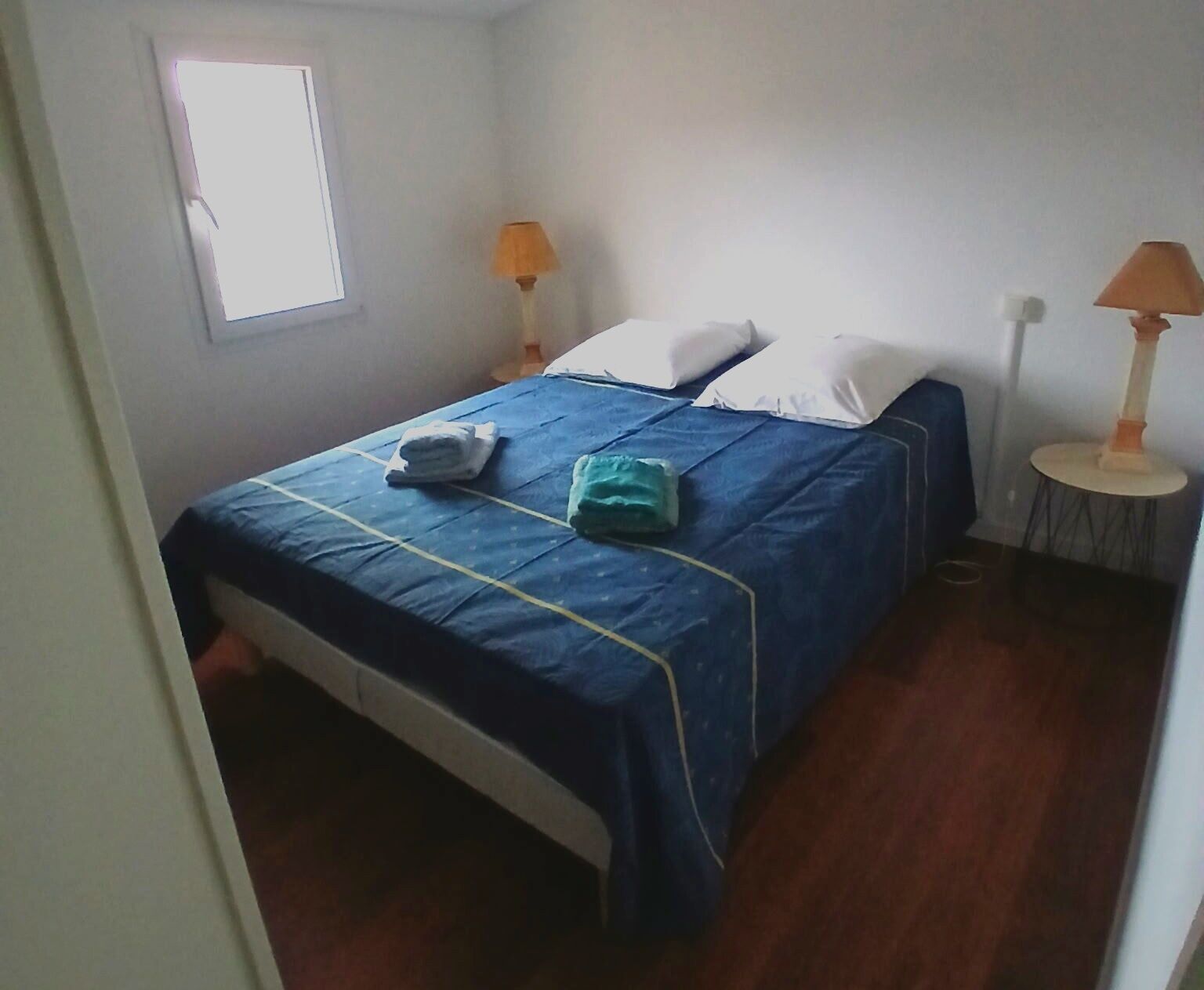 A bedroom with a bed, two bedside lamps, a window, and a door.
