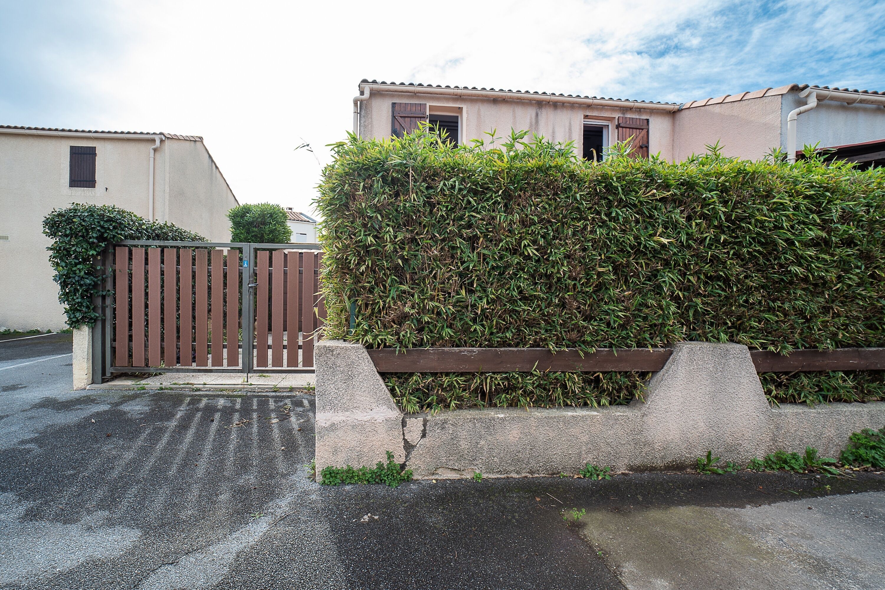 Un edificio residencial con entrada porticada, seto y camino de hormigón.