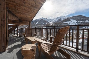 Um deck de madeira com uma mesa e cadeiras, com vista para uma paisagem montanhosa coberta de neve.