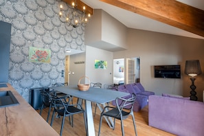 Un salon moderne avec un coin repas, des poutres en bois au plafond et un mur orné de motifs.