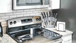 Une cuisine équipée d’une cuisinière en acier inoxydable, d’un four à micro-ondes placé au-dessus et d’un bloc à couteaux posé sur le plan de travail.