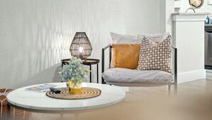 Un salon moderne avec une table basse ronde, un canapé agrémenté de coussins à motifs, un lampadaire en fibres tressées et une petite table d’appoint sur laquelle est posée une plante.