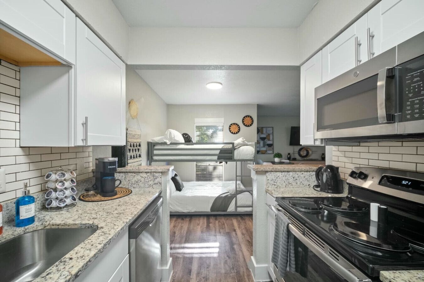 Una cocina compacta con gabinetes blancos, microondas, estufa y pileta.