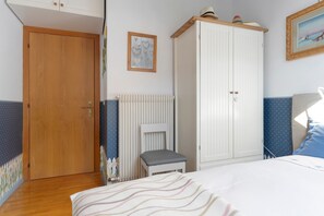 Un dormitorio con puerta de madera, radiador, armario blanco, cama con manta a rayas y almohada azul.