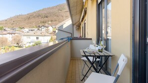 Un balcón con mesa y sillas, una ventana y vistas a un pueblo en la ladera.