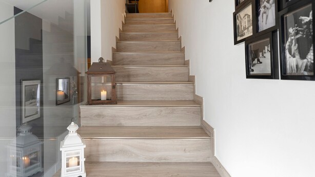 Una escalera de madera con barandilla de cristal y cuadros colgados en la pared.