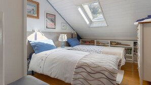 Un dormitorio con dos camas, un tragaluz, una mesita de noche con lámpara y una estantería.