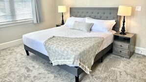 A bedroom with a bed, two bedside tables, a nightstand, a window with blinds, and a carpeted floor. - Rustic Elegance Steps from Bourbon Country (Versailles)