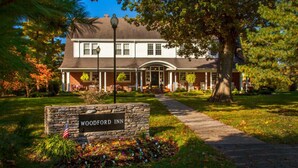 A two-story building with a covered porch and a stone sign reading 'WOODFORD INN'.
