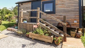 A wooden cabin with a wooden staircase leading to a door, surrounded by gravel and potted plants. - Dunfell Shepherd's Hut (Appleby-in-Westmorland)