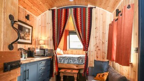 A cozy cabin interior with a kitchenette, a bed with patterned bedding, a blue cabinet, and a patterned rug. - Dunfell Shepherd's Hut (Appleby-in-Westmorland)