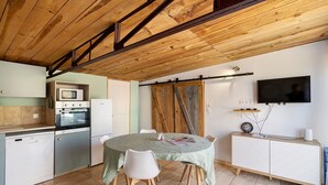 Una cocina con una mesa de comedor, sillas, un televisor y techo de madera.