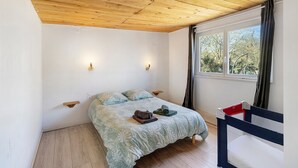 Un dormitorio con techo de madera, una cama con colcha estampada, dos lámparas fijadas a la pared y una ventana con cortinas.