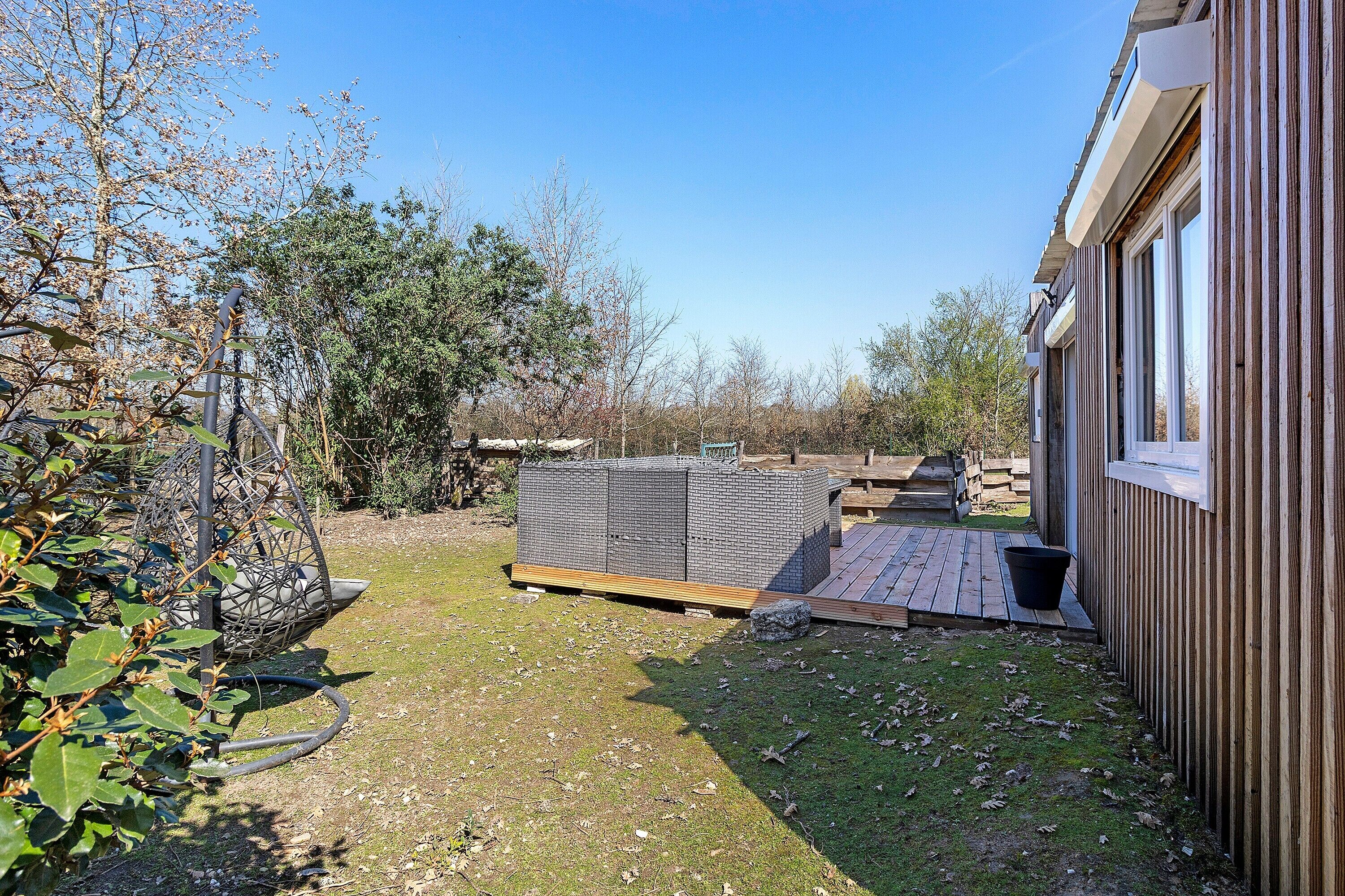 A backyard with a wooden deck, a large storage unit, and a hanging chair.