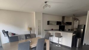 Eine moderne Küche mit Essbereich, darunter ein Holztisch und Stühle, ein eingebauter Backofen und ein Edelstahl-Kühlschrank.