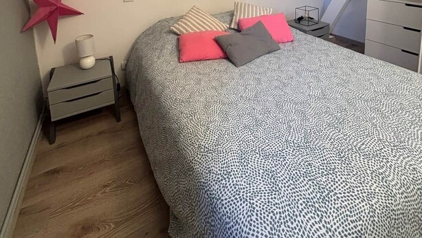 Een slaapkamer met een schuine kap, een bed met beddengoed met een patroon, een nachtkastje met een lamp, een ster decoratie, en een klein bureau met een stoel.