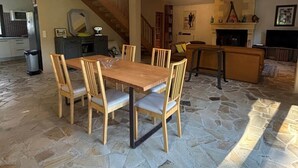 Een ruime woonkamer met een stenen vloer, houten meubels, een open haard en een trap.