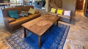 Een ruime woonkamer met een houten salontafel, banken en een kamerkleed met dessin.