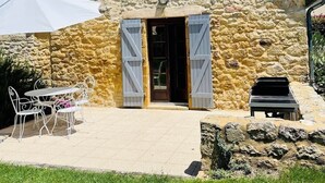 A stone building with a tiled roof, a door with shutters, a small window, and outdoor seating. - Domaine*Charme*Piscine*Domme (Domme)