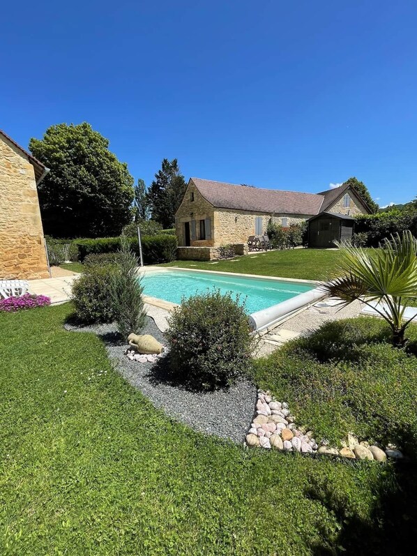 Uma casa de pedra com piscina, cercada por um jardim e relvado bem cuidados.