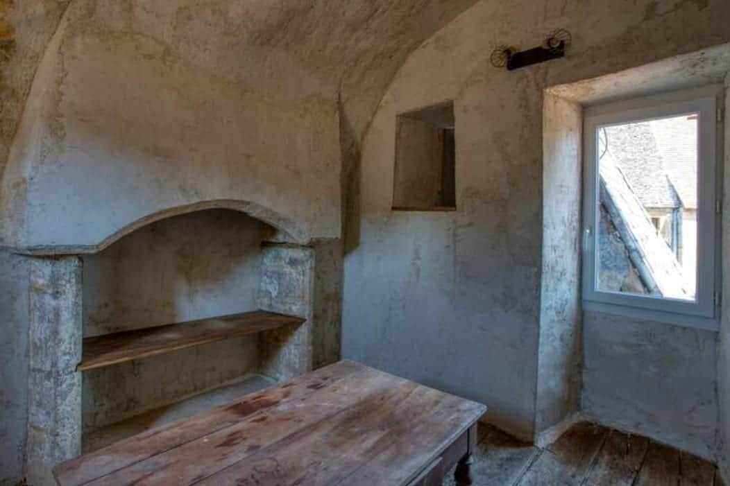 A room with a stone wall, a wooden bench, a small window, and a door.