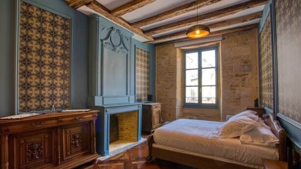 A bedroom with a bed, a fireplace, a window, and wooden beams on the ceiling. - "Betty B's apartments Historic center (Sarlat-la-Canéda)