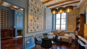 A room with a dining table, chairs, a sofa, a fireplace, and a wall with patterned wallpaper. - "Betty B's apartments Historic center (Sarlat-la-Canéda)
