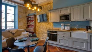A cozy room with a stone wall, a dining area with a table and chairs, a sofa, and a kitchen with cabinets and appliances. - "Betty B's apartments Historic center (Sarlat-la-Canéda)