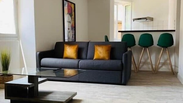 Een moderne woonkamer met een bank, een salontafel en een keukenhoek met barstoelen.