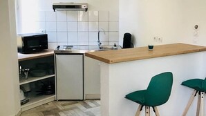 Een kleine keuken met een magnetron, koelkast en een houten bar.