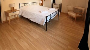 Un dormitorio con cama, mesitas de noche, una silla, vigas de madera y un ventilador de techo.