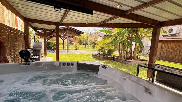 Un jacuzzi bajo un porche cubierto con vista a un patio trasero y una parrilla.