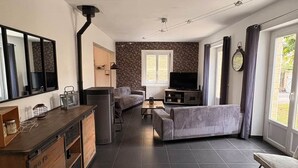 Una sala moderna con un sofá, una mesa de centro y un televisor. Hay una zona de cocina con un refrigerador y un armario de madera.