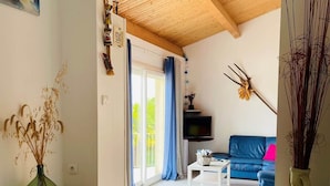 Un salon avec un canapé bleu, une table basse et un téléviseur. Le plafond est en bois et il y a une grande fenêtre avec des rideaux bleus.