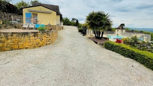 Une allée de gravier mène à une maison dotée d’un mur en pierre, d’une piscine et offrant une vue sur le paysage.