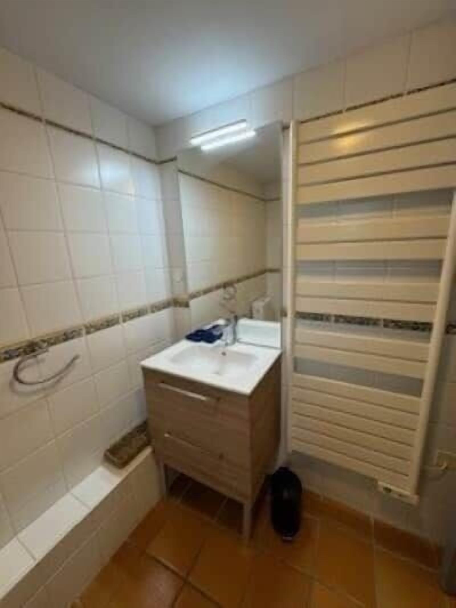 A bathroom with white tiled walls, a white sink, a mirror, a towel rack, and a toilet.
