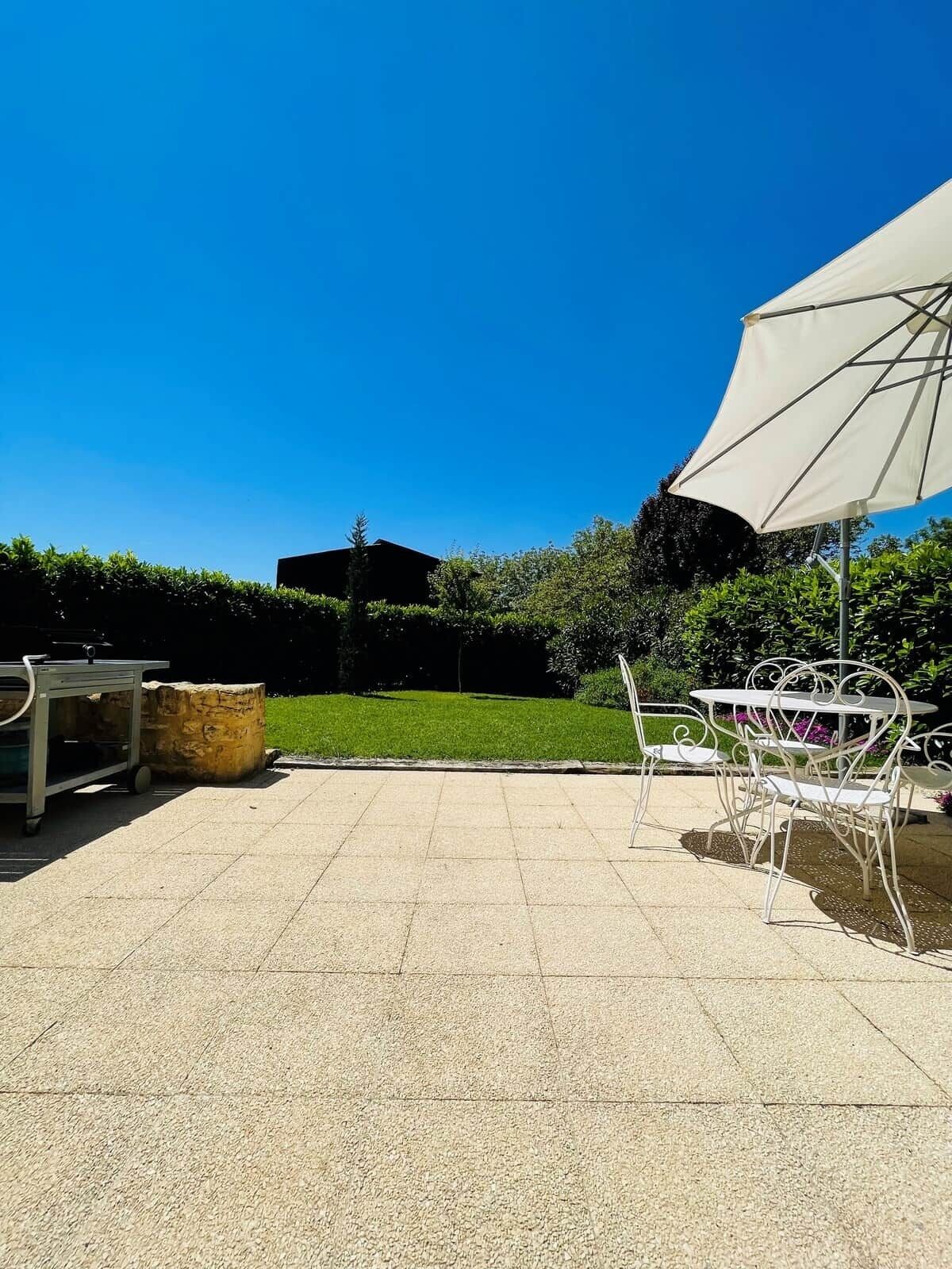 An outdoor patio with a table and chairs, a white umbrella, and a stone planter.