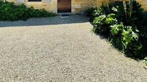 Un bâtiment en pierre avec une allée gravillonnée, une porte en bois et des volets.