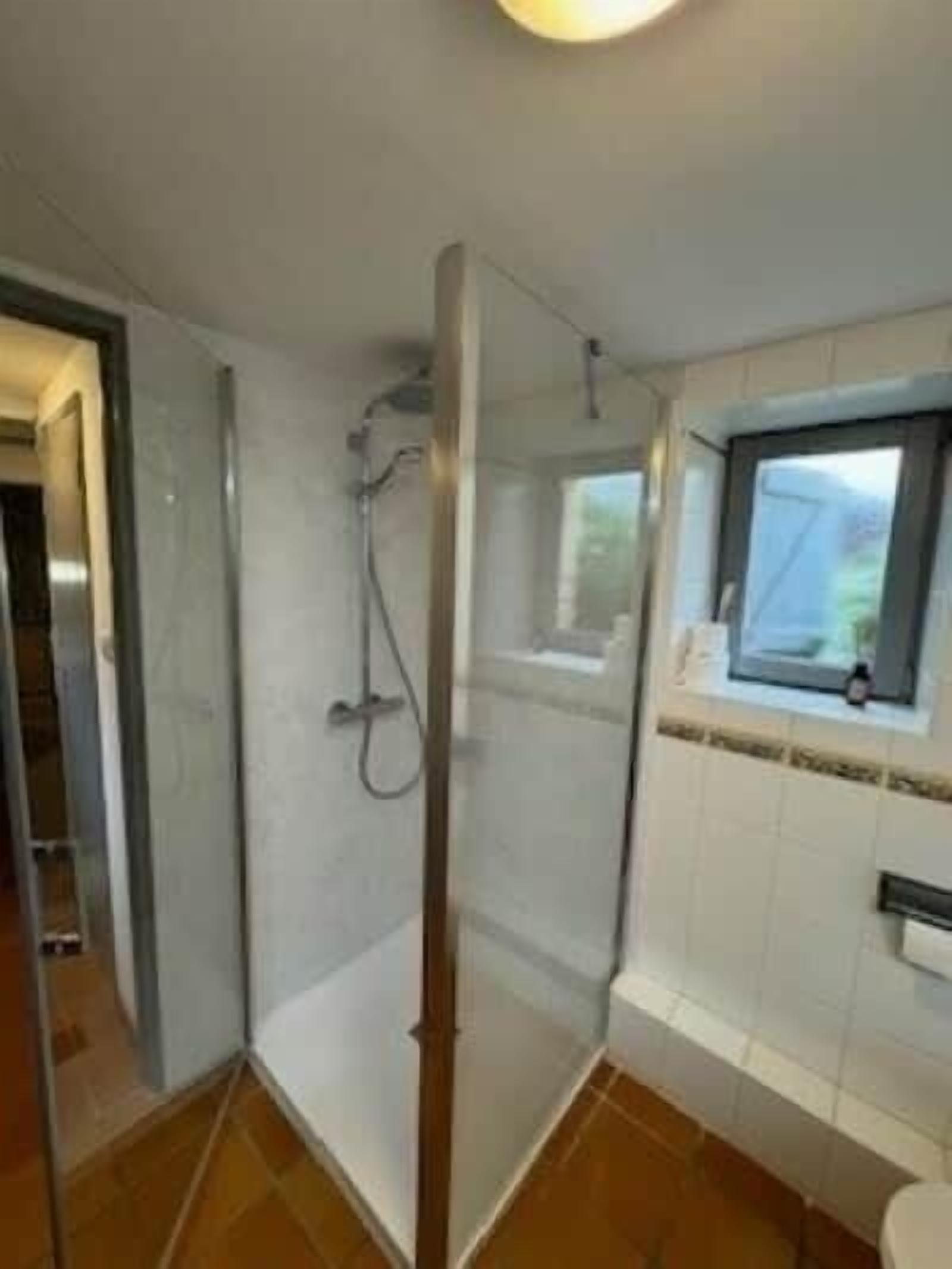 A bathroom with a glass shower enclosure, a window, and a tiled floor.