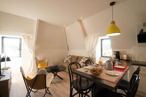 A modern living room with a dining area, a sofa set, a coffee table, and a yellow pendant light. - Maison 8 pers • Pkg • Terrasse • Centre historique (Sarlat-la-Canéda)
